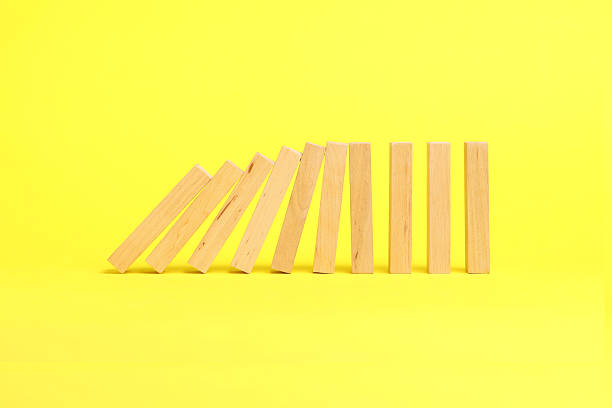 istock Domino effect. Wooden blocks falling on yellow background 2226763221