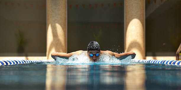 Swimmer performing butterfly stroke in indoor pool with bright lighting