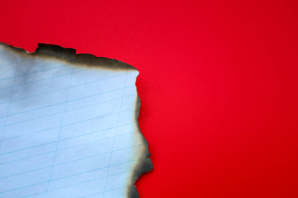 A sheet of checkered paper with burnt edges is placed on a vibrant red background. This image visualizes completion, burning, or transformation, ideal for illustrations on themes of radical change, the past, or loss of information.