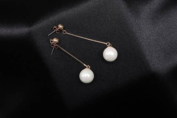 Beautiful pearl earrings on black cloth, top view