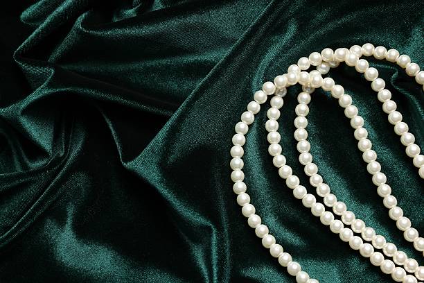 Beautiful pearl necklace on green cloth, top view. Space for text