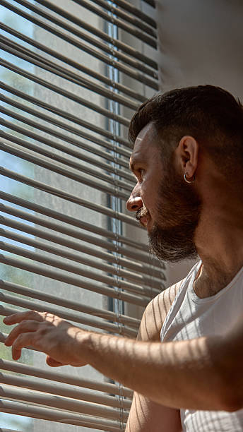 istock Glam shadows. Man sits in partial light, shadow lines from blinds across his face. 2226765034
