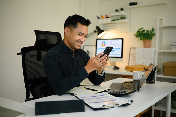 istock Smiling Confident businessman seated at his desk in a modern office while looking at his smartphone 2226767192