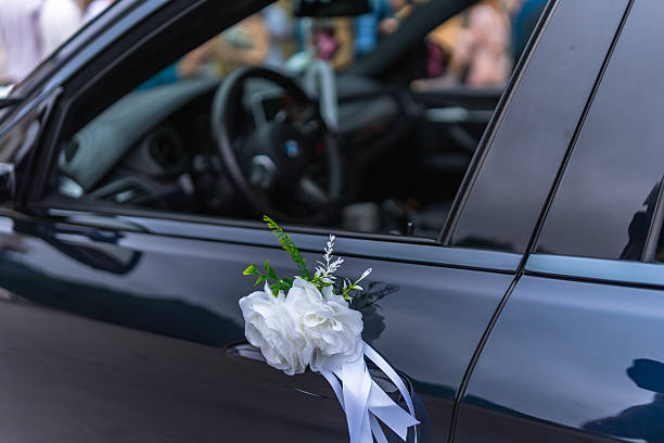 Close-up of white roses and ribbons decorating a car door handle, adding a touch of elegance to a wedding celebration