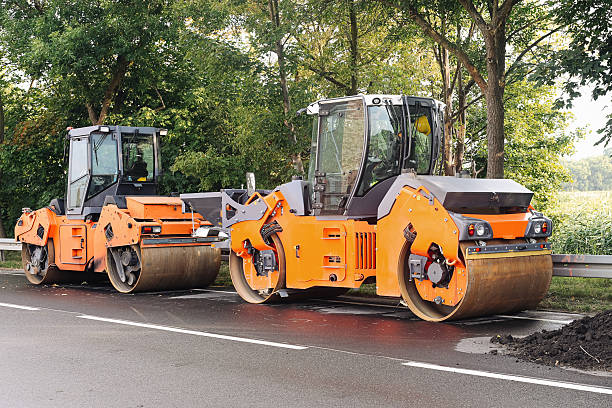 istock Road construction machinery parked. Two orange asphalt rollers. Freshly paved surface. Modern heavy equipment on roadside. 2226780802