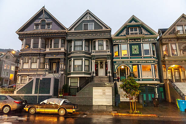 San Francisco, California, USA - June 15, 2024: Row of vibrant Victorian-era houses lines a San Francisco street. Central building, painted blue with white trim, features ornate details including bay windows, decorative moldings, and grand entrance. Neighboring houses in pastel shades complete picturesque scene, exemplifying city's famous 'Painted Ladies' architectural style. Scene captures essence of San Francisco's unique residential charm and historical preservation.