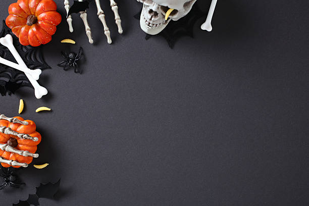 Dark Halloween flat lay with skull, crossed bones, pumpkins, bats, spiders, skeleton hands, and yellow worms