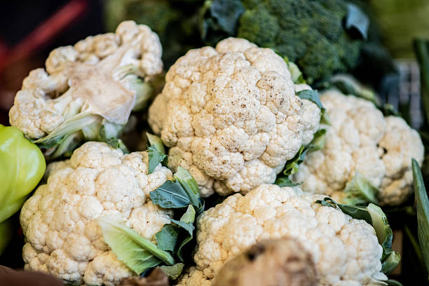 A pile of fresh cauliflower heads stacked neatly at a farmers market stall, highlighting their texture and crispness.