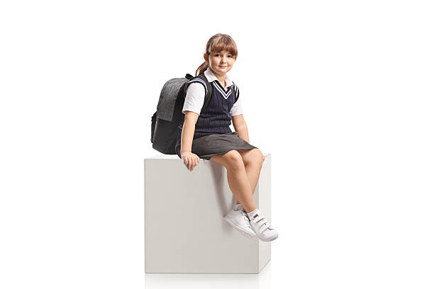istock Girl in a school uniform sitting on a white cube 2226790816