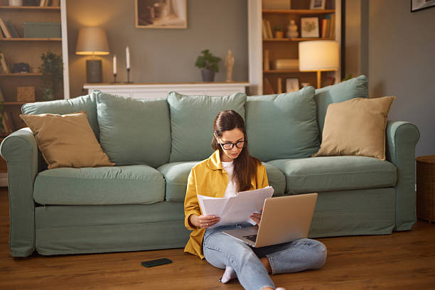 istock Young woman working from home sitting on the floor using laptop and reading documents 2226794302
