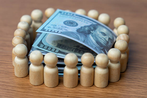 istock A stack of U.S. hundred-dollar bills surrounded by a wooden human figurines. 2226795728