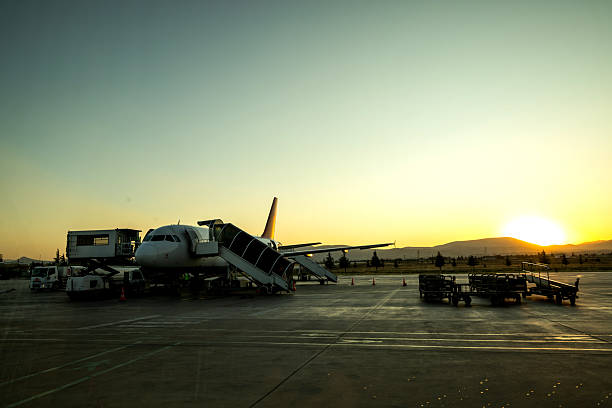 An airliner parked on the tarmac bathed in golden hour light, with soft clouds and warm tones in the background.