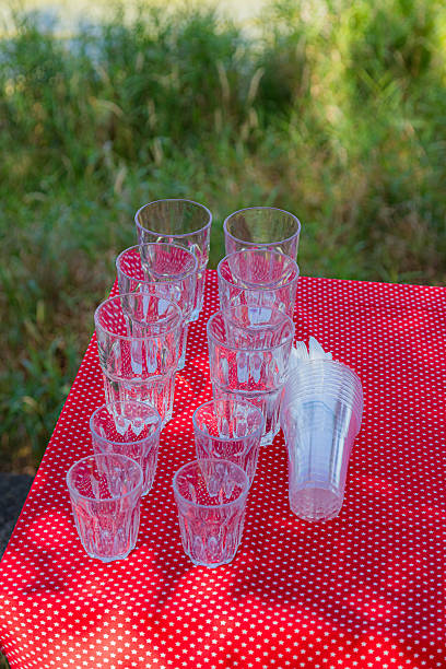 A collection of various clear glass and plastic cups are neatly arranged on a vibrant red tablecloth adorned with small white stars, ready for a gathering.