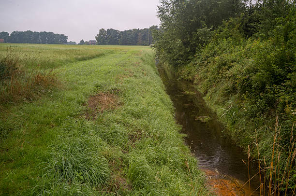 istock Drainage ditch running through green fields in overcast weather 2226807917