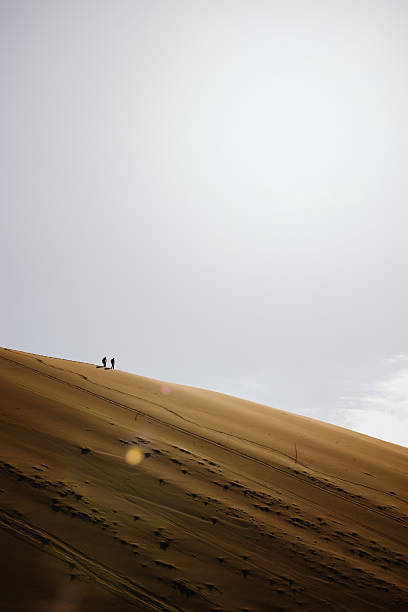 istock Two hikers walking on a sand dune in the desert under cloudy sky 2226811458
