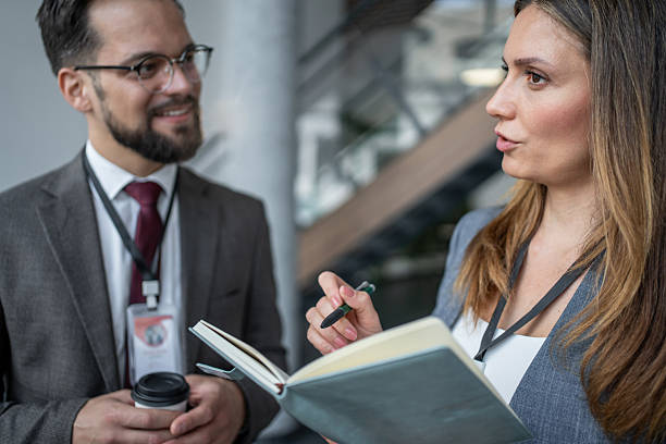 Businesswoman holding a notebook and pen. Jotting down notes while attentively listening to a businessman during an engaging conference or business meeting. Fostering collaboration and communication