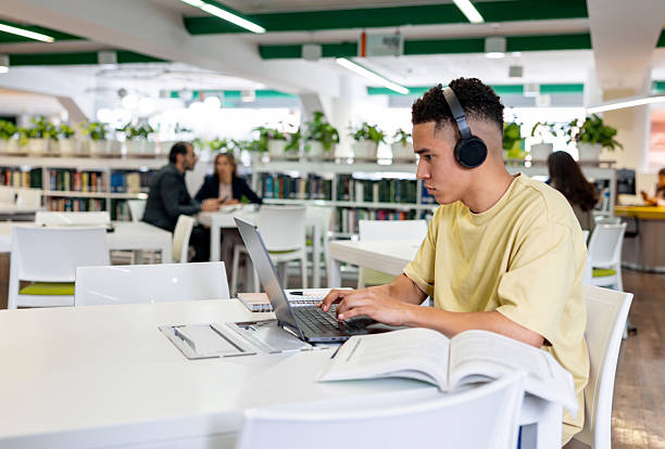 istock University student at the library using headphones while studying on his laptop 2226813074