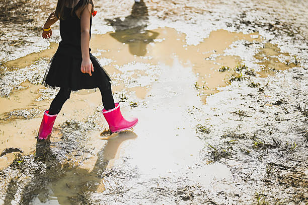 Child with pink boots walking in a mud puddle
