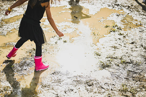 Child walking in a mud puddle wearing pink rubber boots