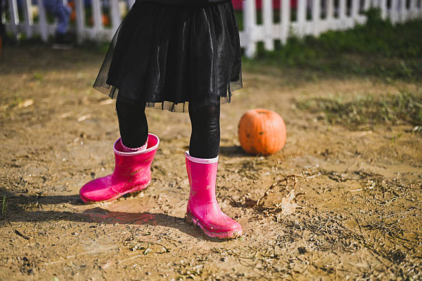 istock Child with pink boots standing near a pumpkin in mud 2226815530
