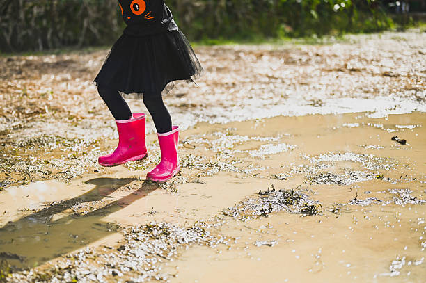 istock Child with pink rain boots jumping in a mud puddle 2226815541