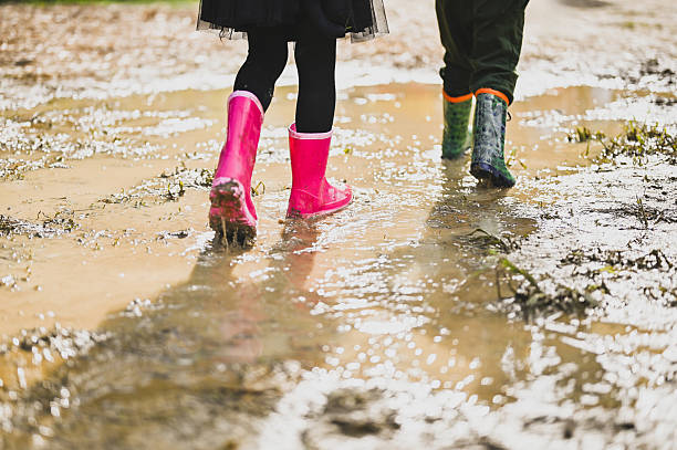 Two children having fun walking in a muddy puddle in rubber boots