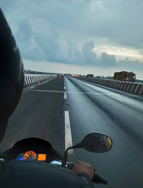 istock This image captures a first-person perspective of someone riding a motorcycle on a wet highway, likely after or during a rain shower, as evidenced by the water drops on the mirror and the wet road surface. 2226815809