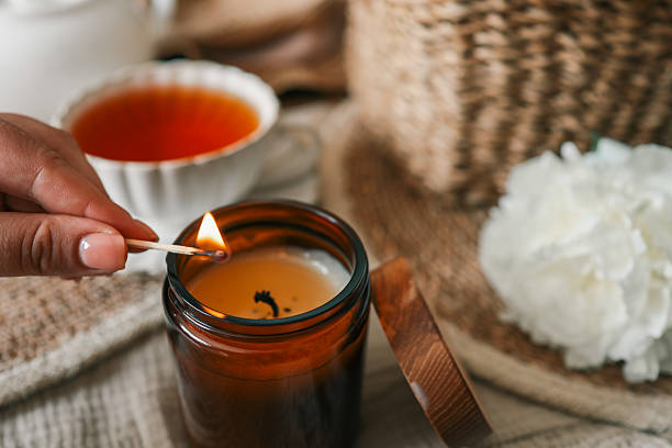 istock Hand lighting a candle in a cozy flat lay scene with tea, white peonies, straw hat, and an open book. Warm summer moment of relaxation and self-care in soft natural light 2226823113