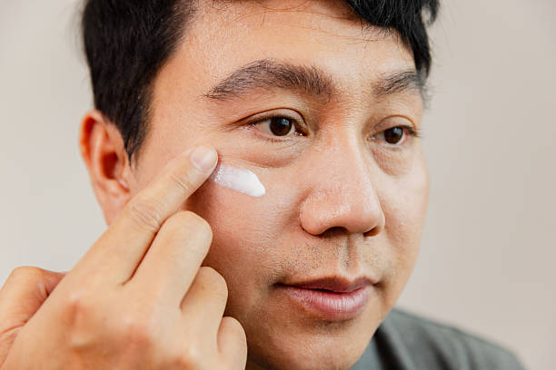 istock Man applying face cream during skincare routine in a bright indoor setting with a neutral background 2226823516
