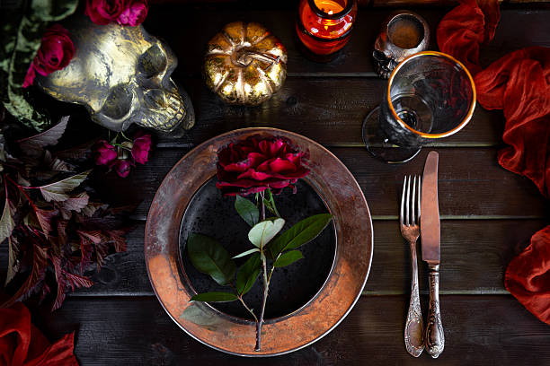 Served table with autumn decor, red roses, scull and pumpkin. Halloween dinner table setting top view