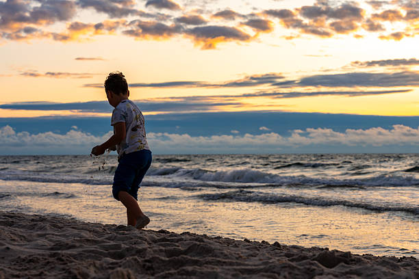 A young boy enjoying sandy seashore at dusk, tossing sand while waves crash nearby, symbolizing childhood, freedom and peaceful beach time