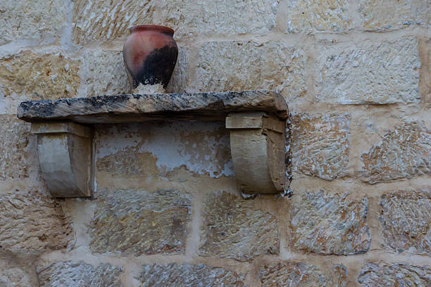 A decorative clay jug displayed on a rustic stone shelf mounted against a rough-textured wall, creating a warm and earthy ambiance with a vintage feel, perfect for illustrating historic or traditional themes.