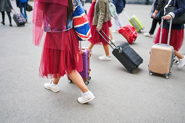 Group of young female tourists in matching red skirts arriving at a train station with rolling suitcases