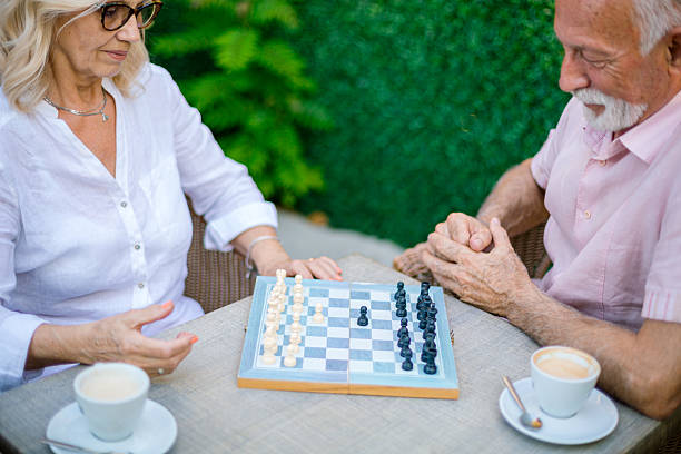 Concentrated senior couple playing chess and drinking coffee at a table outdoors
