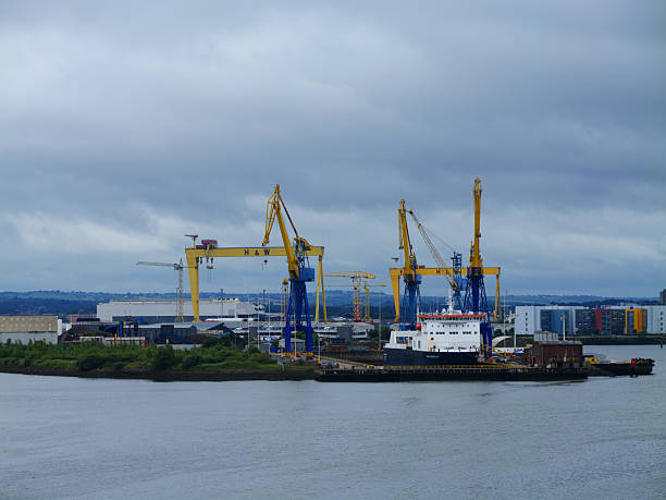 Belfast, UK - Jun 15 2025: The formidable Harland and Wolff cranes tower over the shipyard in Belfast, UK, under a dramatic cloudy sky.