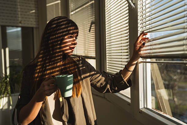 istock Beautiful young woman holding mug and moving blinds 2226842072
