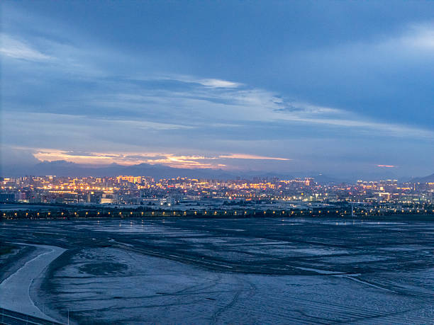 A serene coastal city skyline illuminated against a twilight sky, capturing the transition from day to night. The calm sea in the foreground adds tranquility to the urban backdrop.
