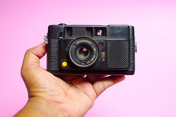 istock A hand holding a vintage black camera against a soft pink background providing a retro photography 2226862924