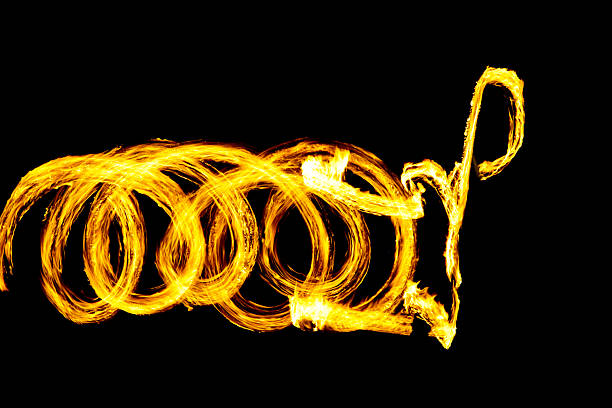 This image captures a stunning fire spinning performance, showcasing luminous circles and swirling patterns against a stark black
