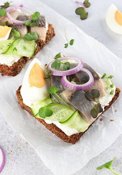 Danish smorrebrod with herring, egg, cucumber, onion on rye bread on white background. Close up