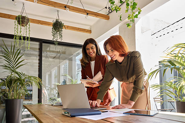 Two happy professional female partners working in office looking at laptop.