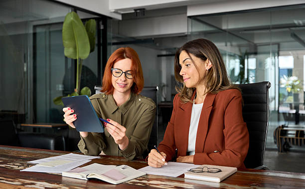 istock Two busy business women talking using tab working together at desk in office. 2226866430