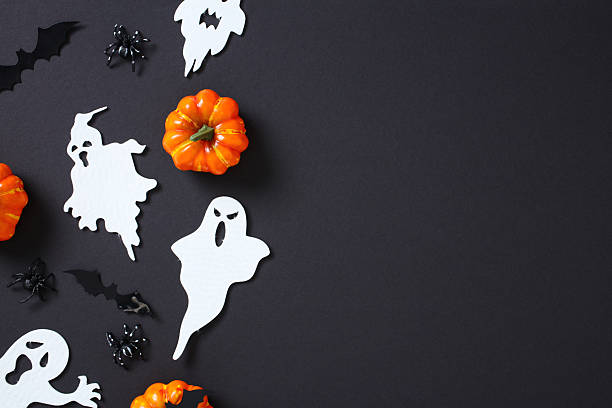 Halloween decorations on black background: pumpkins, ghosts, bats, and spiders arranged creatively for spooky festive ambiance