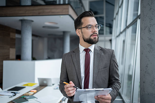 istock Businessman holding clipboard and pen looking out office window 2226869142