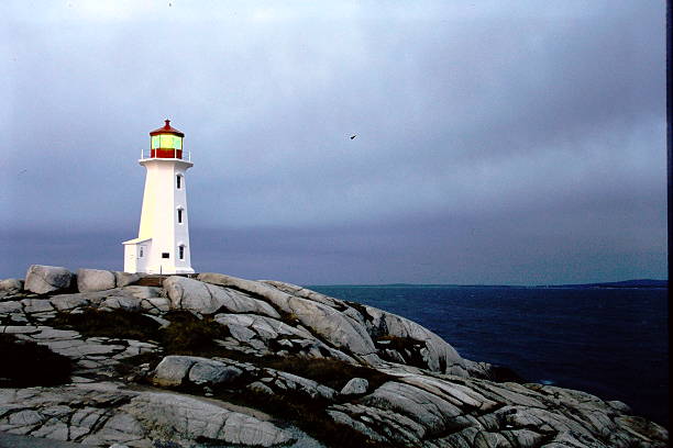 Peggy’s Cove Lighthouse silhouetted during a vivid Atlantic sunset, captured on 35mm slide film in 2001. The warm tones and subtle grain evoke a nostalgic, timeless feel of Nova Scotia’s rugged coastline.