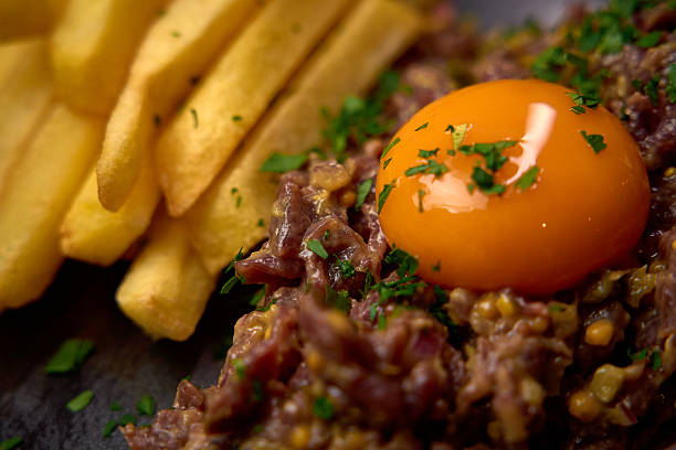 istock Deliciously Prepared Plate Featuring Raw Beef Tartar with a Bright Yellow Egg Yolk and Crispy French Fries Garnished with Fresh Herbs 2226872246