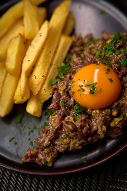 istock A delectable dish featuring a rich meat tartare topped with a vibrant egg yolk, accompanied by crispy golden fries and fresh herbs on a stylish plate. 2226872405