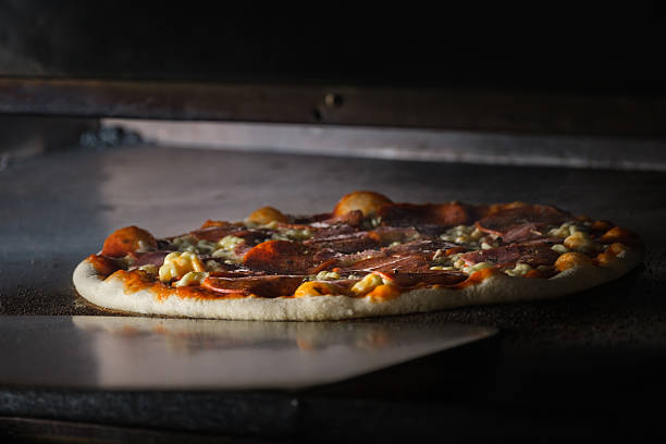 Round pizza featuring pepperoni and gooey cheese baking on a metal tray inside a professional oven, creating a delicious aroma