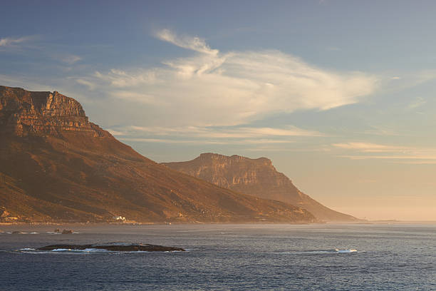 A coastal scene featuring dramatic mountains during a tranquil evening. The interplay of soft light and wispy clouds creates a sense of calm and beauty. Perfect for backgrounds and scenic depictions.