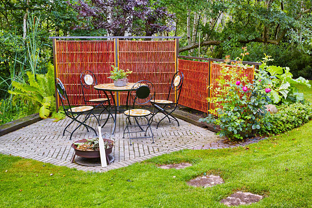 istock Charming Danish garden setting with an iron dining set amidst lush greenery and vibrant flowers, surrounded by a rustic privacy screen 2226877959